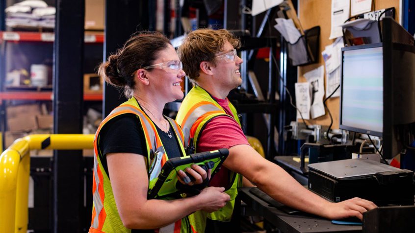 Two warehouse workers entering data into a computer